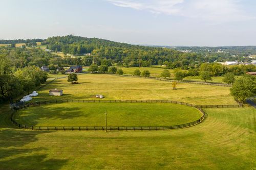 Aerial view of a large fenced oval paddock bordered by open pasture and a distant town