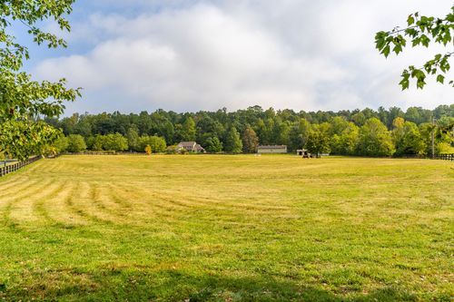 Freshly mown pasture bordered by a wood fence with a farmhouse and barn in the distance