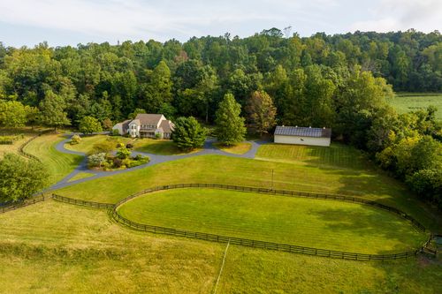 Aerial view of a two-story home with a fenced pasture and outbuilding near the tree line
