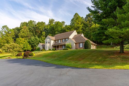 Two-story shingle and brick home set on a sloped lawn with mature trees