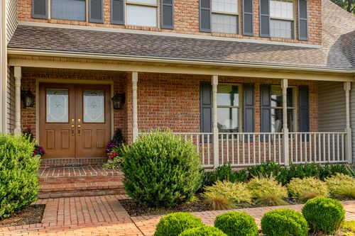 Brick home exterior with a covered wraparound porch, shutters and double front doors