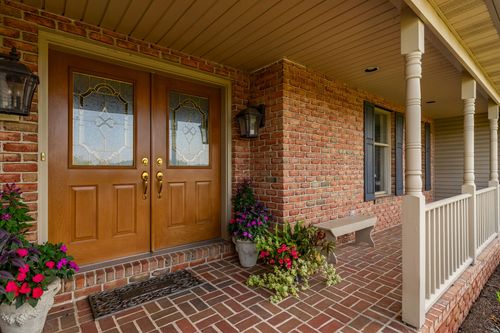 Covered brick porch entry with double wood doors flanked by potted flowers