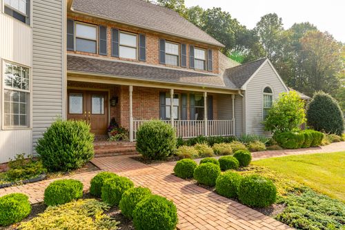 Brick two-story home entrance with covered porch and landscaped brick walkway