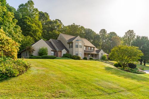 Tan two-story home on a sloped lawn framed by mature trees