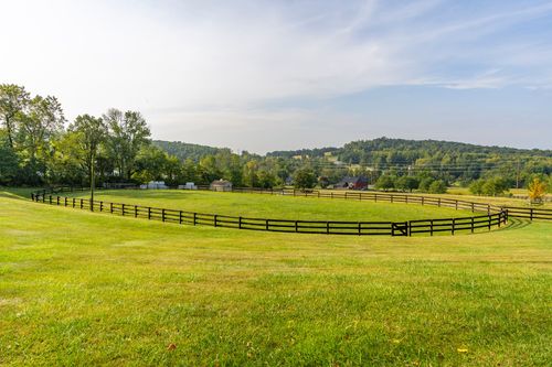 Black wood fence enclosing an oval pasture with rolling hills in the background