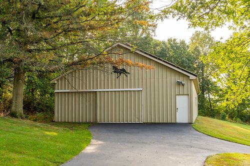 Side view of a tan pole barn with a horse decal and wide paved apron