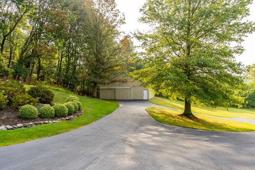 Driveway curving past a large pole barn framed by mature shade trees