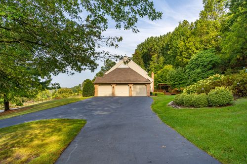 Paved driveway leading to a three-car garage beneath a wooded hillside
