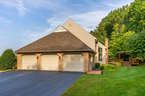 Brick and shingle three-car garage with a paved driveway and a deck visible beyond