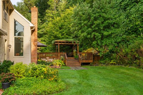 Wood deck with pergola and brick chimney backs up to a lush, tree-lined yard