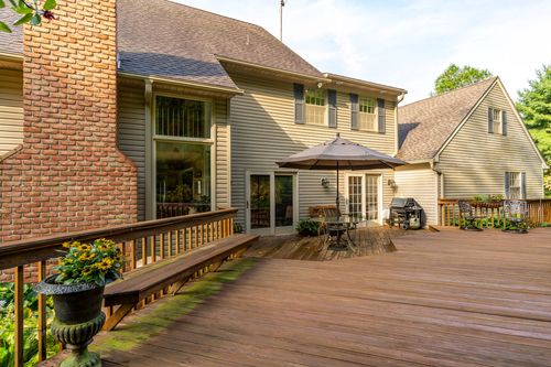 Multi-level wood deck with umbrella table and grill wraps around a shingle-and-brick home