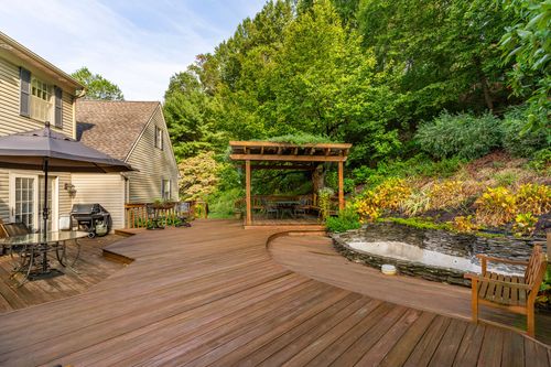 Expansive wood deck leads to a pergola-covered dining area beside a stone-edged garden pond