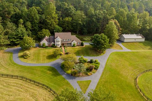 Aerial view of a two-story home with circular driveway, mature trees and open lawn