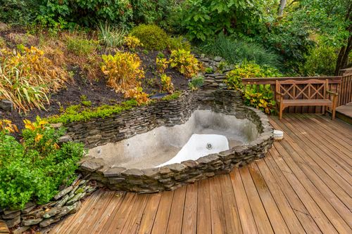 Empty stone-lined pond feature framed by autumn plantings on a wood deck