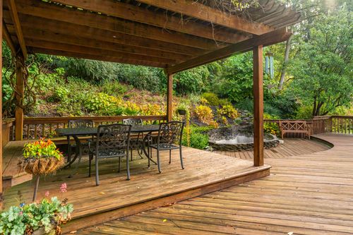 Pergola-covered outdoor dining area with wrought iron table and chairs overlooking a garden pond