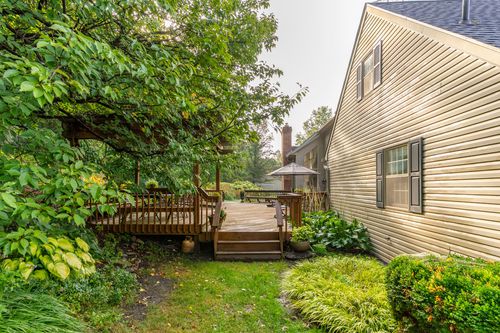 Wood pergola deck tucked beside the home with a brick chimney rising through the trees