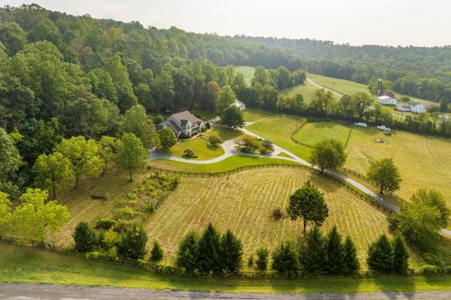 Aerial view of a home with a wooded hillside backdrop and fenced pasture beyond