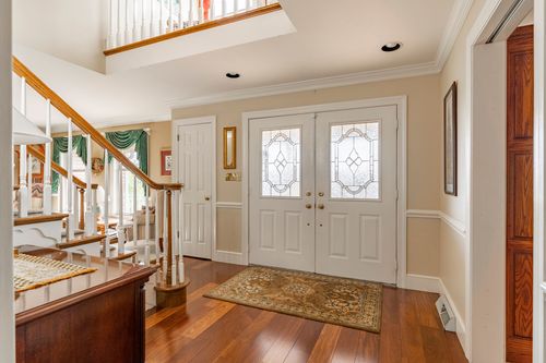 Two-story foyer with double glass-paned front doors, a wood staircase, and hardwood floors