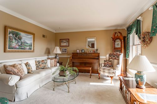 Living room with a cream sectional sofa, wingback chair, grandfather clock, and upright piano