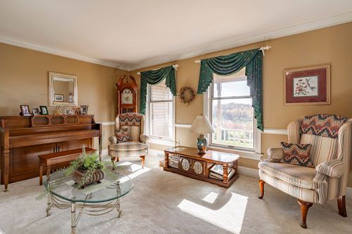 Living room with a piano, striped wingback chairs, and teal drapery framing garden-view windows