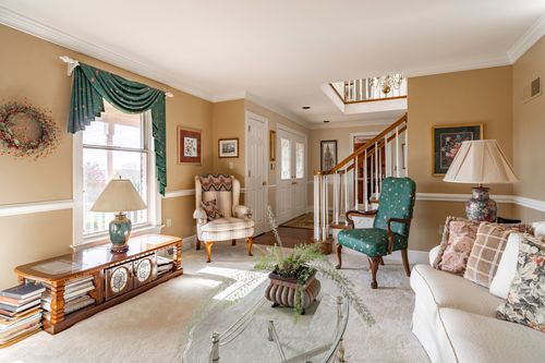 Open living room with a teal accent chair, cream sofa, and staircase visible beyond