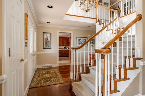 Foyer with a white staircase, wood banister, wrought iron chandelier, and runner rug