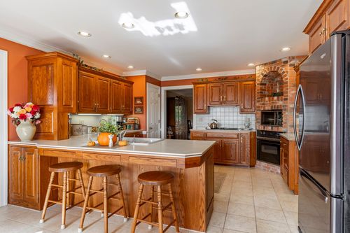 Kitchen with a brick oven surround, orange walls, and an island with three wood bar stools
