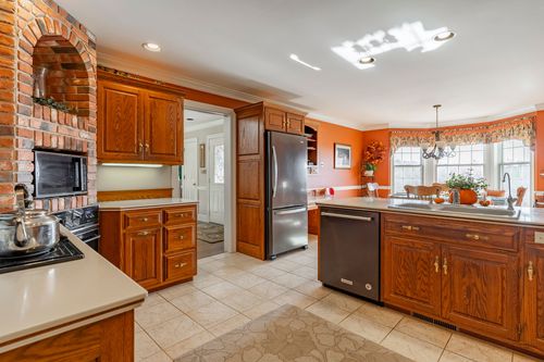 Kitchen with a brick accent wall, stainless refrigerator, and a bay-window breakfast nook beyond