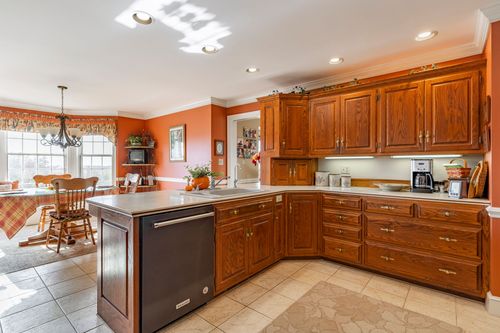 Kitchen island with a black dishwasher and oak cabinetry opens to a chandelier-lit breakfast nook
