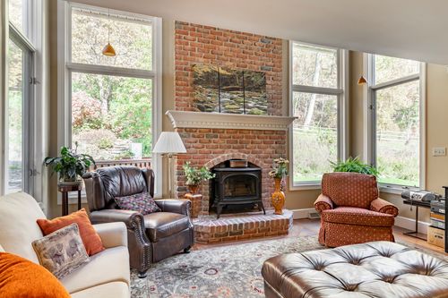 Vaulted family room with a brick fireplace, wood stove insert, and a cream sofa with orange accent pillows