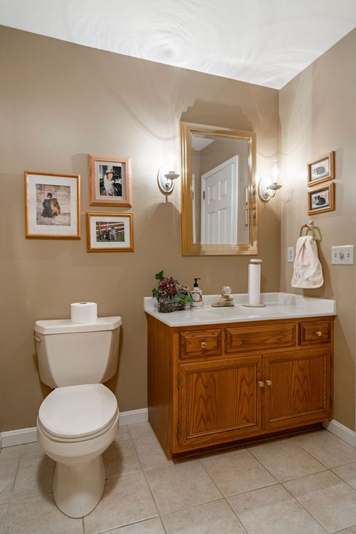 Powder room with an oak vanity, gold-framed mirror, and a gallery wall of family photos