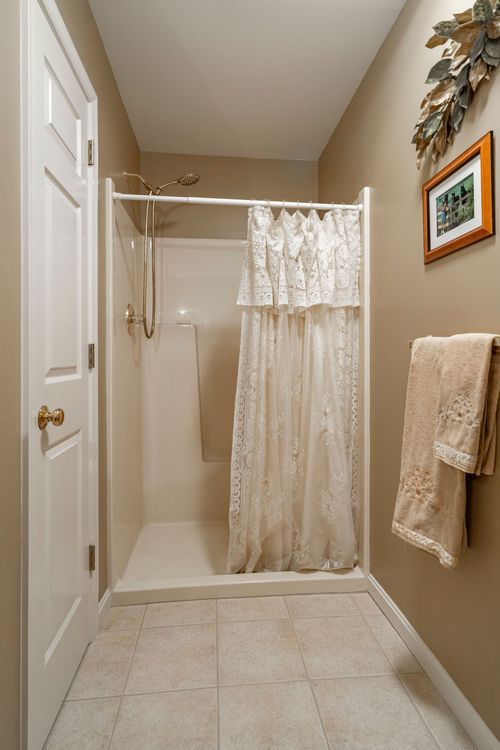 Bathroom with a tiled walk-in shower, lace curtain, and tan towels