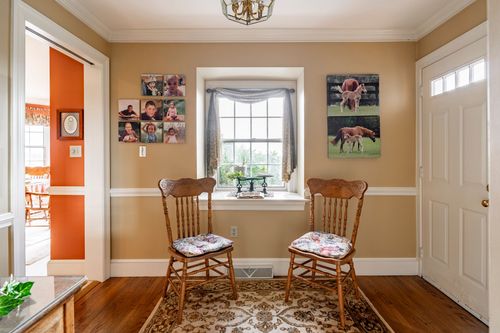 Small sitting nook with two wood chairs, framed farm-animal photos, and a window bench