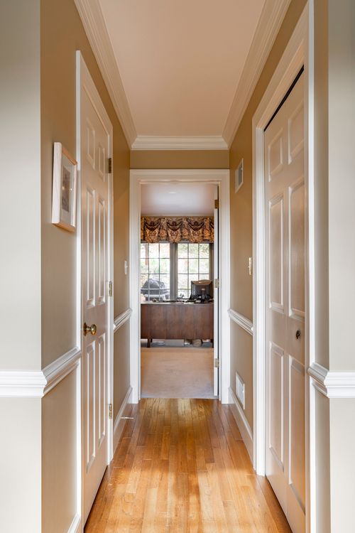 Upstairs hallway with wood flooring leads to a home office with a patterned window valance