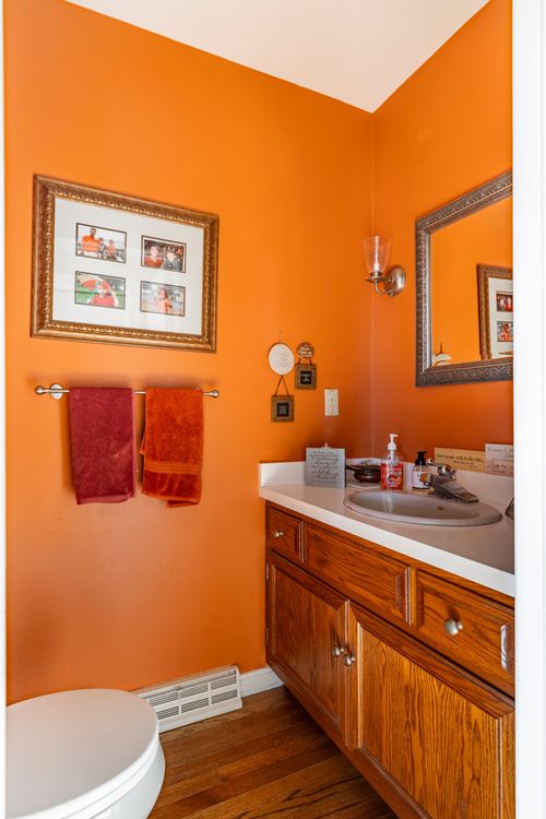 Bright orange powder room with an oak vanity and coordinating towels