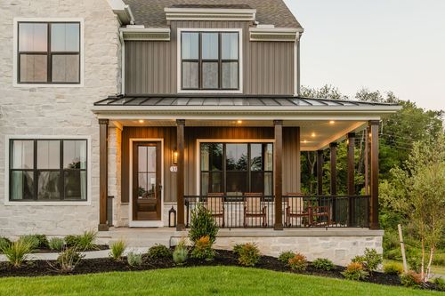 Covered front porch with a stone base, wood columns, and a metal roof at dusk