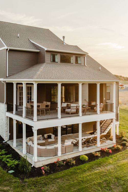 Two-story covered rear porch with wicker furniture overlooks open fields at sunset