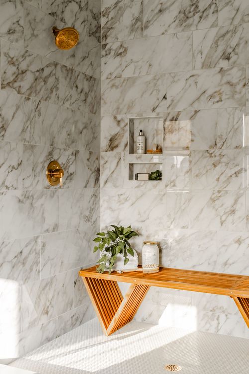 Walk-in shower corner with marble tile, a brass shower head and built-in niche shelves
