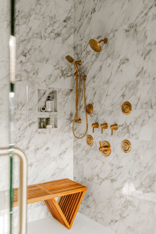 Walk-in shower with an array of brass shower heads, controls and a teak slat bench