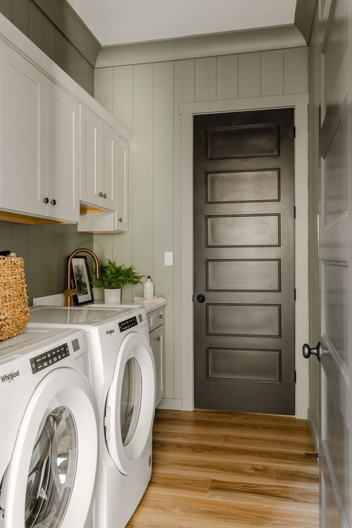 Laundry room with white cabinetry, a dark paneled door and wide-plank wood flooring