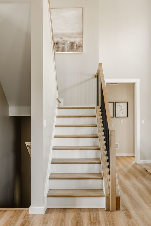 Wood staircase with black metal balusters and framed abstract art on the landing wall