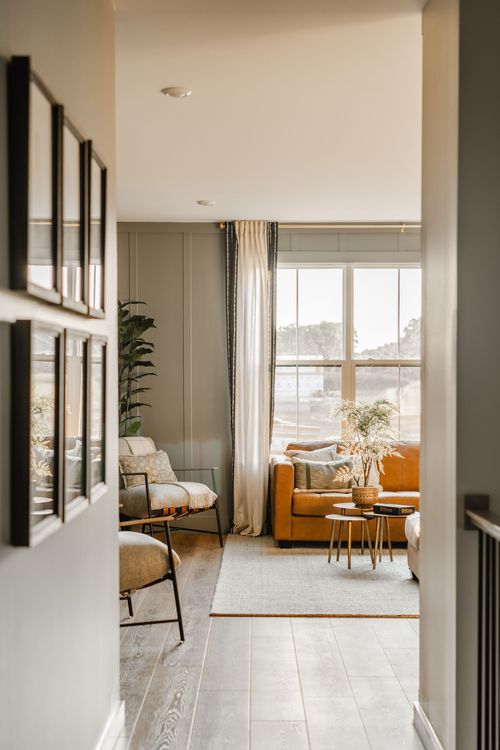 Sage-paneled sitting area with a leather sofa, gallery wall and tall window