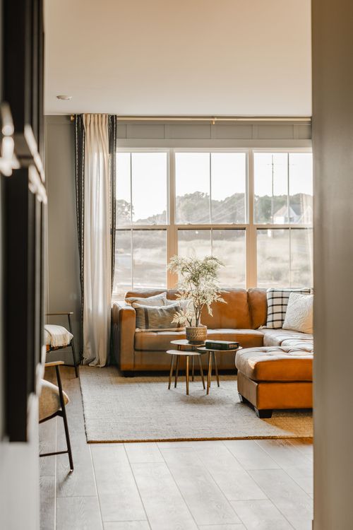 Living room with a tan leather sectional and floor-to-ceiling windows overlooking fields