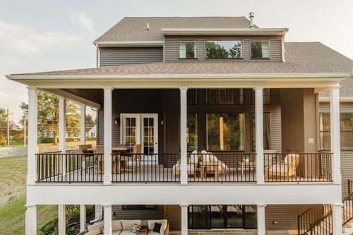 Two-level covered porch with wicker seating and French doors at golden hour