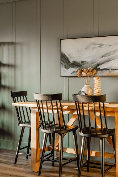 Dining nook with a wood table, black spindle-back chairs and an abstract landscape painting