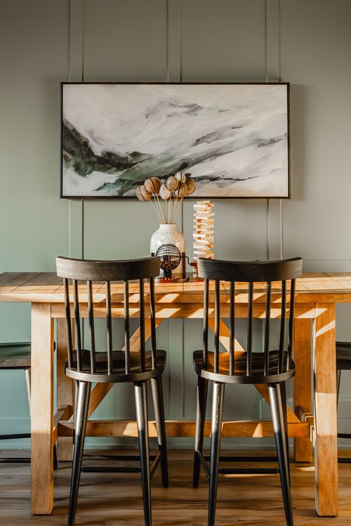 Dining table close-up with black spindle chairs, wood table and abstract wall art