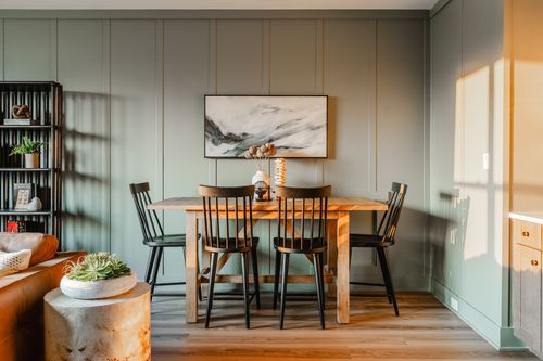 Dining area with a wood table, black chairs and sage paneled walls