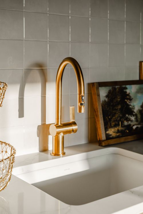 Close-up of a brass gooseneck faucet over a white stone sink with a framed painting