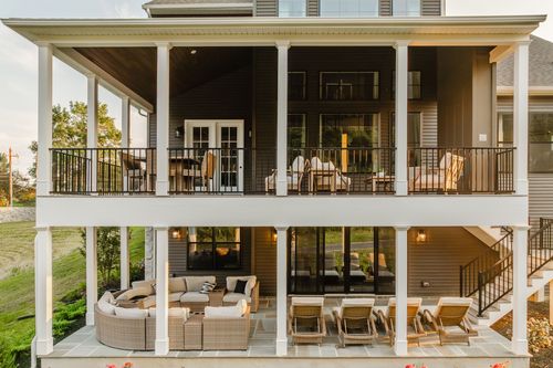 Stacked covered porches with wicker furniture and a stone patio below