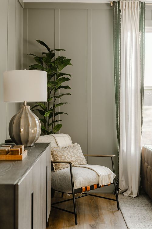 Sitting nook with olive paneled walls, a table lamp, potted plant and striped curtain